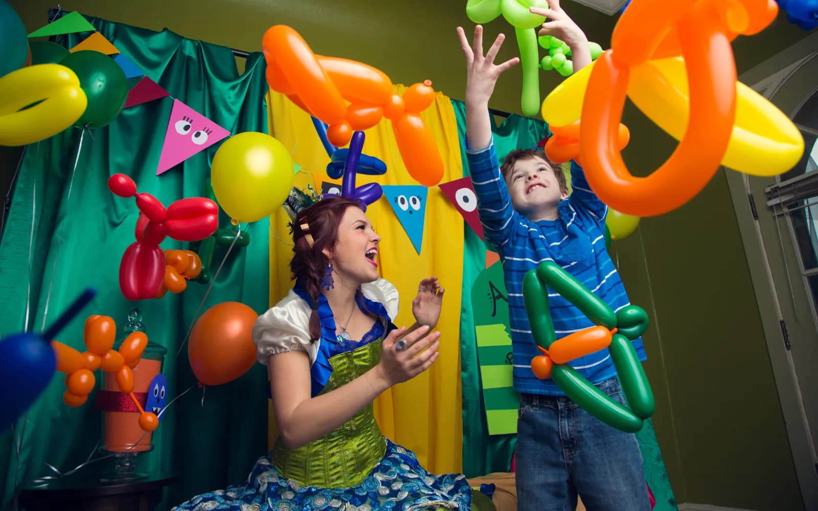 A Happily Ever Laughter balloon twister makes a balloon animal for a smiling child at an outdoor party while other children look on.