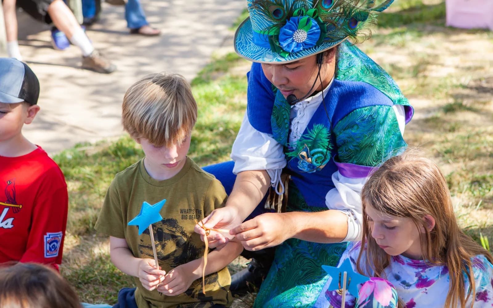 A Happily Ever Laughter craft leader helping a smiling child make a craft at an outdoor party while other children work alongside.