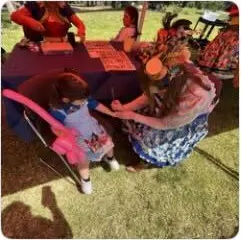 A child seated at a craft table making art with a Happily Ever Laughter faerie at an outdoor event.