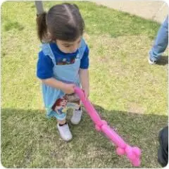 A young child on a grassy lawn holding a long pink balloon sword.