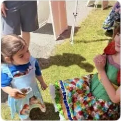 A toddler in costume beside a Happily Ever Laughter performer in a floral dress outdoors.