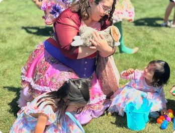 A Happily Ever Laughter faerie holding a small child while another child sits nearby on a lawn.