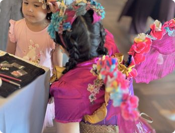 A faerie performer in a pink costume with a young child at an indoor event.