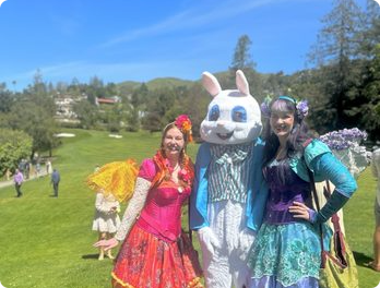 Two Happily Ever Laughter faeries and a person in an Easter bunny costume on a golf-course lawn.