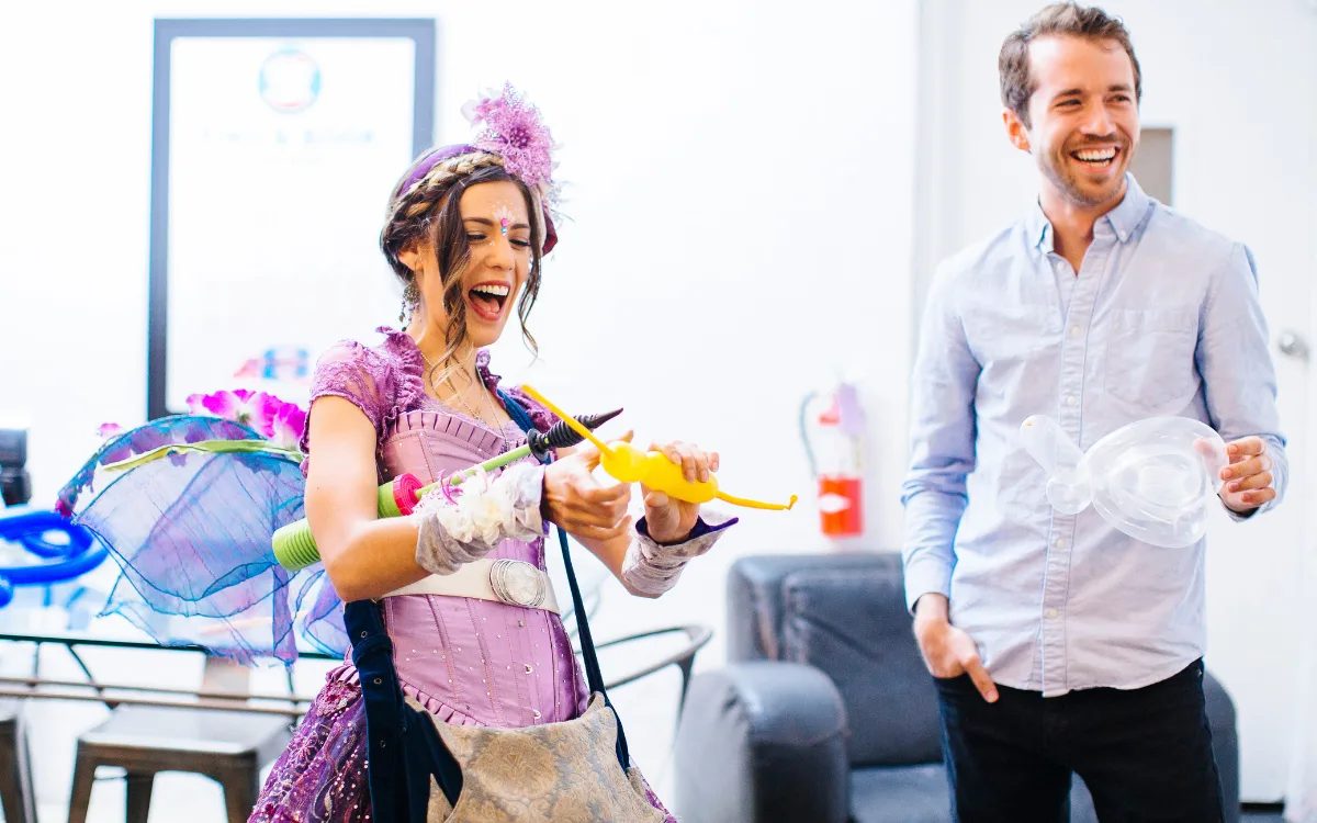 A Happily Ever Laughter balloon twister roaming an outdoor party handing balloon animals to children.