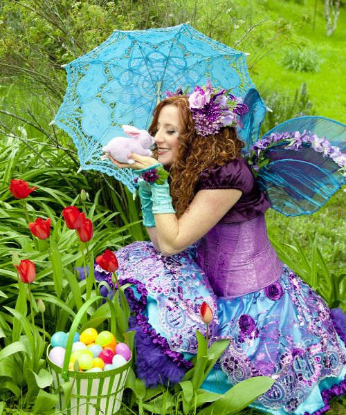 Fairy performer from Happily Ever Laughter posing with a pastel umbrella and a stuffed bunny amidst vibrant tulips and a basket of colorful Easter eggs. Perfect for Easter entertainment, springtime parties, and whimsical events in California.