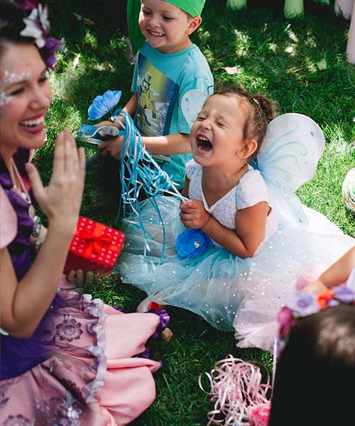 Joyful child dressed as a fairy laughing during a magical performance by a Happily Ever Laughter entertainer, surrounded by children enjoying outdoor party activities. Ideal for showcasing engaging kids' party entertainment and whimsical experiences in California.